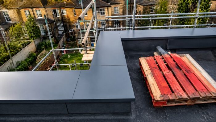 Parapet Wall Coping: The Complete UK Guide to Materials, Types, Installation and Specification 6 Rooftop corner detail showing dark parapet wall coping with scaffolding and flat roof surface