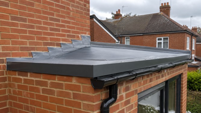 Roof Accessories: A Practical Guide for UK Roof Projects 7 Roof accessories on a modern UK brick building with green roof edge trim, dark aluminium fascia