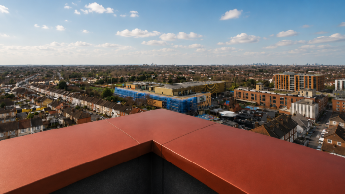 Aluminium Coping Detail: A Practical UK Guide to Wall Tops and Roof Edges 7 Close-up aluminium coping detail showing red coping with rain droplets on a UK rooftop beside scaffolding.