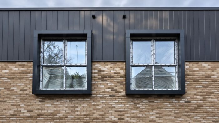 Aluminium Window Surrounds: A Complete Guide to Choosing the Right Exterior Detail 6 Dark grey aluminium window surrounds framing two windows with protective film on a brick and clad facade