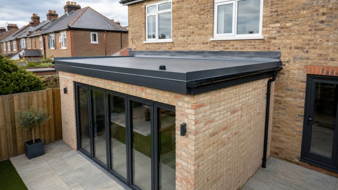 Roof accessories on a new UK brick extension with dark aluminium roof edge trim, wall flashing, black guttering and downpipe