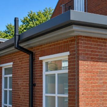 Box Gutter Material installed along the roofline of a brick educational building with covered outdoor access